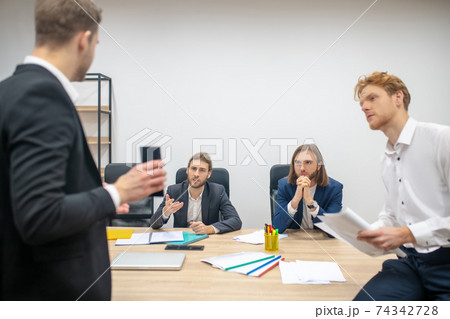 Serious men at table listening attentively to their colleague Serious men at table listening attentively to their colleague 74342728