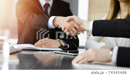 Businessman shaking hands with his colleague above the glass desk in sunny modern office, close-up. Unknown business people at meeting 74343486