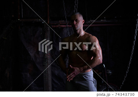 Young shirtless muscular man standing among metal chains, looking at camera, copy space Young shirtless muscular man standing among metal chains, looking at camera, copy space 74343730