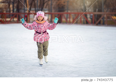 Girl uncertainly stands on figure skates on an ice rink and tries to ride 74343775