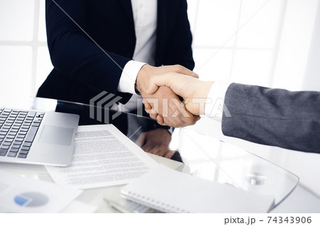 Unknown diverse business people are shaking hands finishing up meeting at the desk in office, close-up. Handshake concept 74343906
