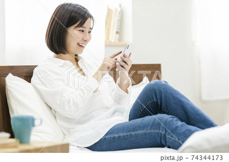 ベッドの上でスマホを操作する若い女性 74344173