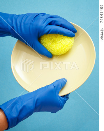 Women's hands in protective gloves with sponge and plate on blue background. Women's hands in protective gloves with sponge and plate on blue background. 74345409