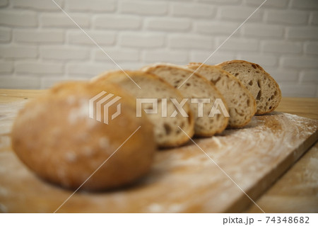 Bread sliced and freshly baked on a wooden table. Flour, bakery. The cooking process is captured in 4k resolution. White brick background. Selective Focus 74348682