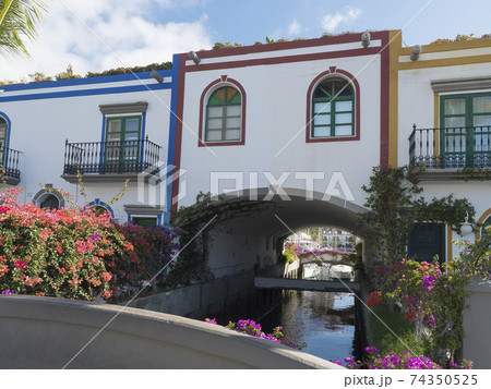 Colorful buildings of Puerto de Mogan with sea canal and boat and flowers. Traditional colonial architecture of small fishing village port, favorite tourist place. Gran Canaria, Canary Islands, Spain Colorful buildings of Puerto de Mogan with sea canal and boat and flowers. Traditional colonial architecture of small fishing village port, favorite tourist place. Gran Canaria, Canary Islands, Spain 74350525
