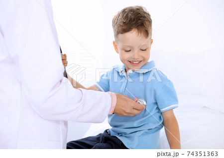 Happy little boy having fun while is being examine by doctor by stethoscope. Health care, insurance and help concept Happy little boy having fun while is being examine by doctor by stethoscope. Health care, insurance and help concept 74351363