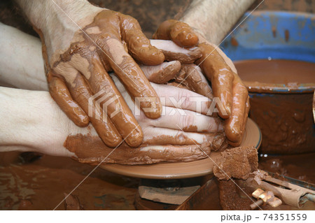 A Craftwoman's hands guiding a other hands, to teach him to work with the ceramic wheel. A Craftwoman's hands guiding a other hands, to teach him to work with the ceramic wheel. 74351559