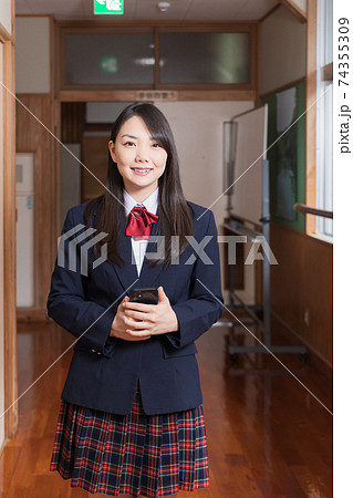 スマホを持って廊下に立っている女子高生 高校生 生徒の写真素材