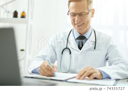 Cheerful doctor doing paperwork and using laptop in clinic 74355727