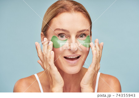 Smiling mature female with under eye moisturizing patches in studio 74355943
