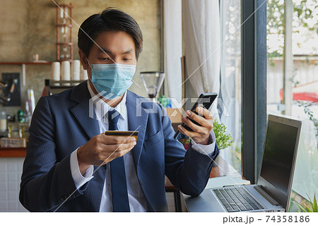 Zoom View Front Sitting Asian Businessman Wear Face Mask Online Shopping by Smartphone Zoom View Front Sitting Asian Businessman Wear Face Mask Online Shopping by Smartphone 74358186