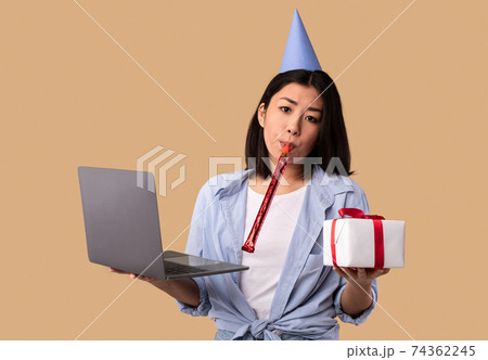 Upset Asian Woman In Hat Holding Present Box And Laptop 74362245