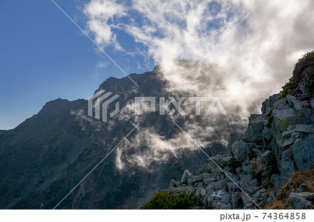 信州、北アルプス、北穂高岳山頂から奥穂高岳、青い空、白い雲。岩陵帯。登山道の白色ペンキの止の文字。 74364858