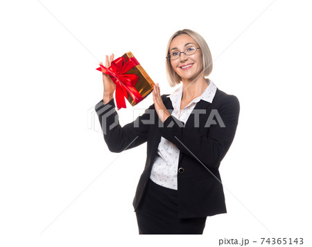 Adult caucasian friendly smiling woman in eyeglasses and formal wear with a red gift box in her hands, isolated on white 74365143