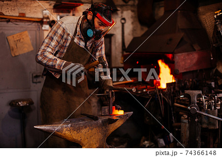 The blacksmith manually forging the molten metal on the anvil in smithy with spark fireworks. 74366148