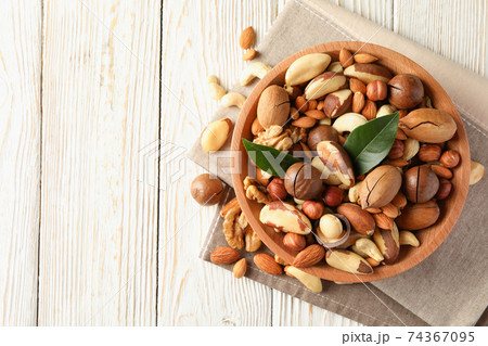 Bowl with different tasty nuts on white wooden background 74367095