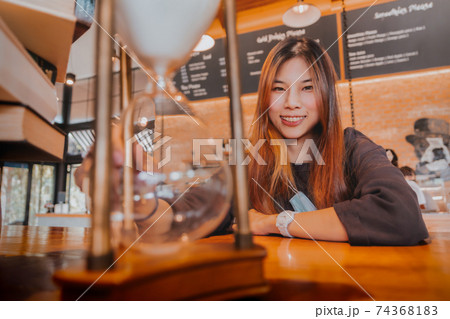 Beautiful asian young female is sitting before a hourglass counting down with smile for relaxing time concept. 74368183