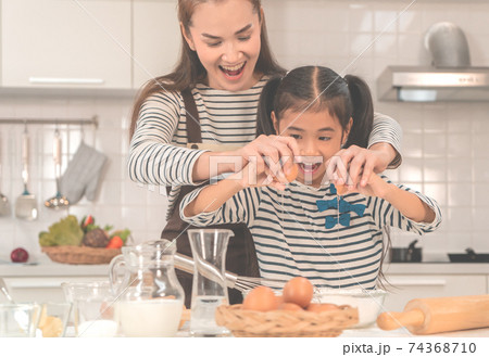 Happy Asian Mother and Daugther is breaking egg to make Bakery in kitchen together, for family fun activity concept. Happy Asian Mother and Daugther is breaking egg to make Bakery in kitchen together, for family fun activity concept. 74368710