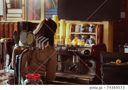 View from the back of female barista preparing coffee in professional coffee machine View from the back of female barista preparing coffee in professional coffee machine 74369573