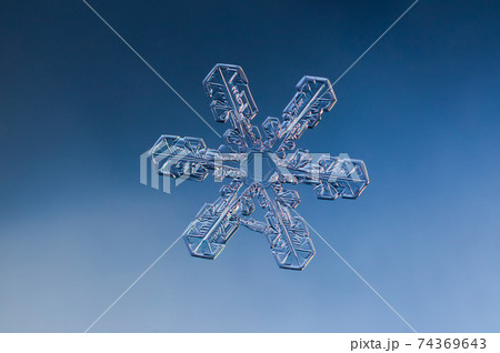 Snowflake on smooth gradient background. Macro photo of real snow crystal on glass surface. This is small snowflake with unusual pattern. 74369643