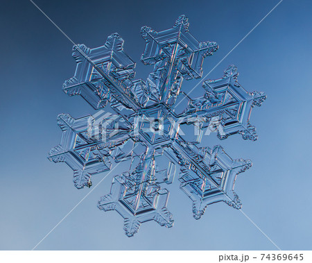Snowflake on smooth gradient background. Macro photo of real snow crystal on glass surface. This is small snowflake with unusual pattern. 74369645
