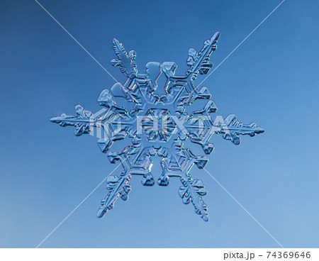 Snowflake on smooth gradient background. Macro photo of real snow crystal on glass surface. This is small snowflake with unusual pattern. 74369646