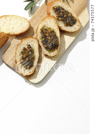 切り分けられたフランスパンの上にナッツ入りのオリーブオイルを塗って食べる(白背景) 切り分けられたフランスパンの上にナッツ入りのオリーブオイルを塗って食べる(白背景) 74375577