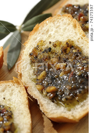 切り分けられたフランスパンの上にナッツ入りのオリーブオイルを塗って食べる(白背景) 切り分けられたフランスパンの上にナッツ入りのオリーブオイルを塗って食べる(白背景) 74375597