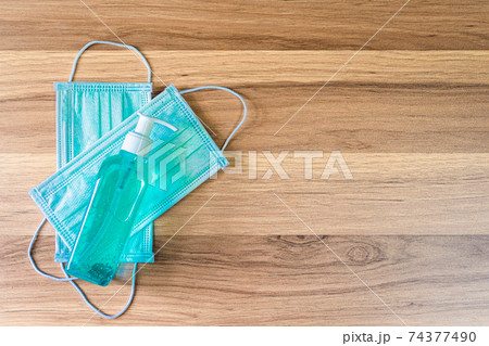 Blue Protective disposable medical mask and alcohol hand sanitizer on wooden background,Top view office table,Concept of Prevention of the spread of COVID-19 virus infection 74377490