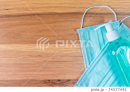 Blue Protective disposable medical mask and alcohol hand sanitizer on wooden background,Top view office table,Concept of Prevention of the spread of COVID-19 virus infection Blue Protective disposable medical mask and alcohol hand sanitizer on wooden background,Top view office table,Concept of Prevention of the spread of COVID-19 virus infection 74377491