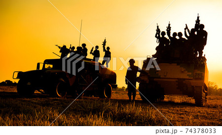 Silhouettes of army soldiers in the fog against a sunset, marines team in action, surrounded fire and smoke, shooting with assault rifle and machine gun, attacking enemy 74378033