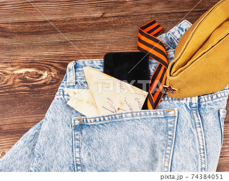 Modern jeans and symbols of victory in the Second World War. St. George's ribbon, military cap, cartridges and letters from the front. The concept of victory on May 9 for a postcard background Modern jeans and symbols of victory in the Second World War. St. George's ribbon, military cap, cartridges and letters from the front. The concept of victory on May 9 for a postcard background 74384051