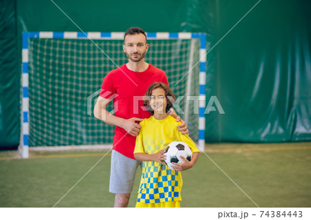 PE teacher in red tshirt standing near his pupil and holding a ball 74384443