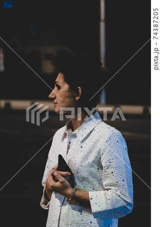 Outdoor portrait of beautiful young woman holding her mobile phone at night. 74387205
