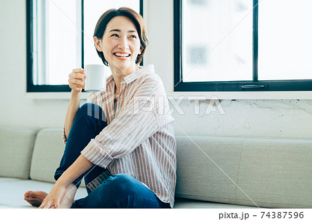 リビングでコーヒーを飲むミドルの女性 リビングでコーヒーを飲むミドルの女性 74387596