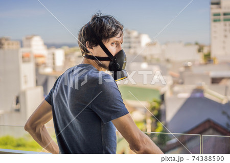 Close up portrait of young man in respirator mask against the background of the city. Man puts on a respirator to protect himself from coronavirus COVID 19 or air pollution Close up portrait of young man in respirator mask against the background of the city. Man puts on a respirator to protect himself from coronavirus COVID 19 or air pollution 74388590