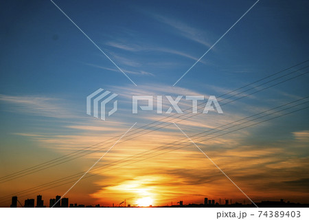 黄金色の太陽が地平線上に姿を現して雲をオレンジ色に輝かせる 74389403
