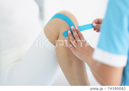 Doctor glues kinesio tape to patient's knee Doctor glues kinesio tape to patient's knee 74390082
