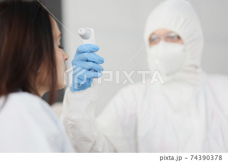 Doctor in protective suit and gloves measures temperature of person Doctor in protective suit and gloves measures temperature of person 74390378
