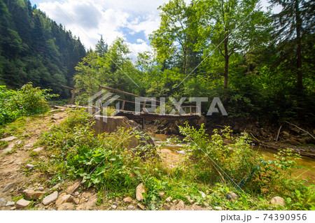 The old wooden weak bridge over small river in mountain forest The old wooden weak bridge over small river in mountain forest 74390956