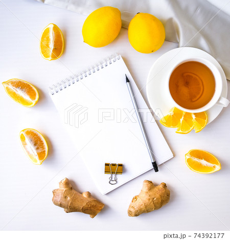 Trendy flat lay Ginger hot immunity boosting Vitamin natural drink With citrus lemon notebook and pencil on white background. Copy space Trendy flat lay Ginger hot immunity boosting Vitamin natural drink With citrus lemon notebook and pencil on white background. Copy space 74392177