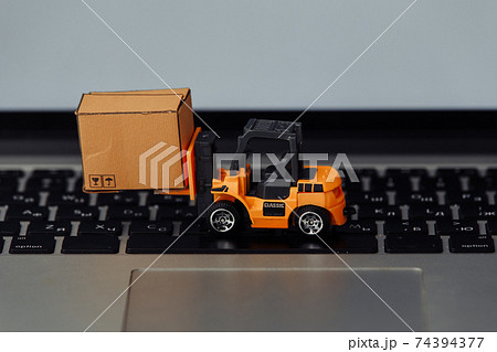 Orange forklift model and carton box on a keyboard. Courier service concept Orange forklift model and carton box on a keyboard. Courier service concept 74394377