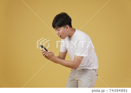 shocked surprised excited young asian man dressed casually looking at mobile smart phone isolated on yellow background shocked surprised excited young asian man dressed casually looking at mobile smart phone isolated on yellow background 74394891