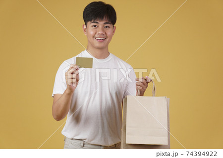 portrait of happy young asian man dressed casually holding shopping bags and credit card isolated on yellow background portrait of happy young asian man dressed casually holding shopping bags and credit card isolated on yellow background 74394922