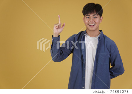 portrait of happy young asian man dressed casually pointing finger up at copyspace. yellow background 74395073