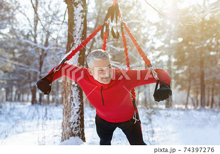 Outdoor bungee fitness. Athletic senior man working out with suspension training straps at snowy winter forest Outdoor bungee fitness. Athletic senior man working out with suspension training straps at snowy winter forest 74397276