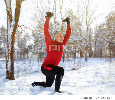 Outdoor functional fitness workout. Mature man using bodyweight resistance straps, doing lunges at snowy winter park Outdoor functional fitness workout. Mature man using bodyweight resistance straps, doing lunges at snowy winter park 74397351