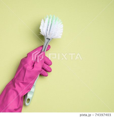 female hand in purple rubber gloves holds a plastic cleaning brush on green background 74397403