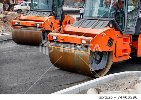 Two large vibratory road rollers compact the fresh asphalt on a new stretch of road. Two large vibratory road rollers compact the fresh asphalt on a new stretch of road. 74400596