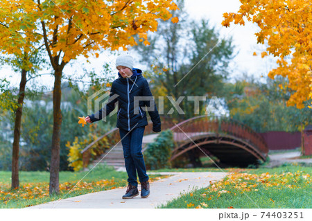 a girl walks along the path and enjoys autumn, maples with yellow leaves and a bridge over the river a girl walks along the path and enjoys autumn, maples with yellow leaves and a bridge over the river 74403251